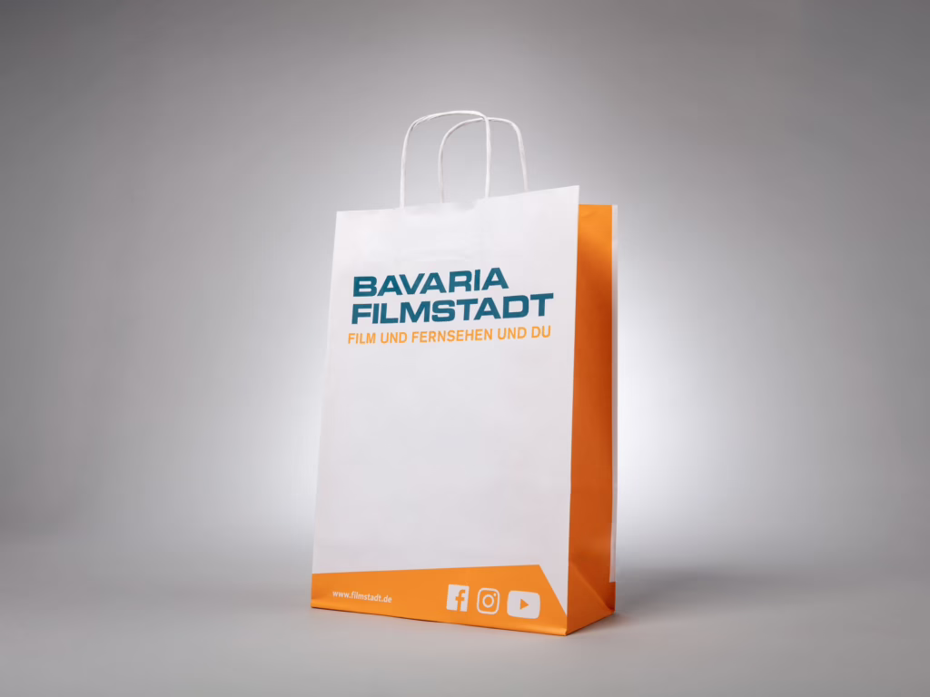 Weiß-orange Papiertragetasche mit gedrehter Papierkordel für Bavaria Filmstadt – bedruckt von Paolo Sandro